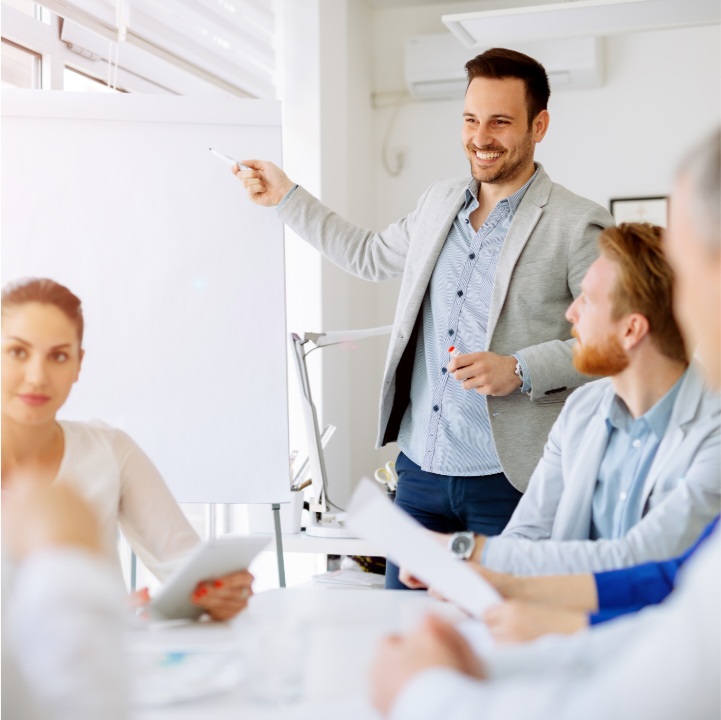 Ein Mann am Flipchart. Eine Frau und zwei weitere Männer unterschiedlichen Alters, die sich austauschen.